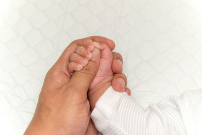 Close-up of parent and baby holding hands on bed