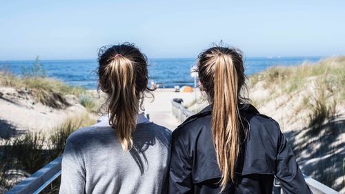 Rear view of female friends at beach against sky
