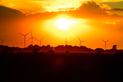 Silhouette of wind turbines on land during sunset