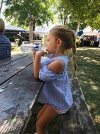 Side view of girl drinking water from bottle while sitting on bench