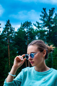 Portrait of woman holding sunglasses against trees