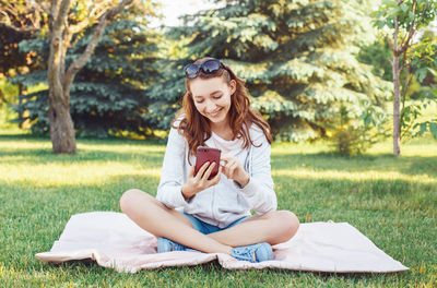 Young woman sitting on grass against trees