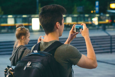 Rear view of man photographing with mobile phone in city