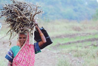 Senior woman carrying firewood on field