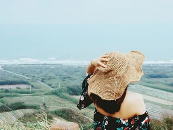 Rear view of woman wearing hat looking away standing against sky