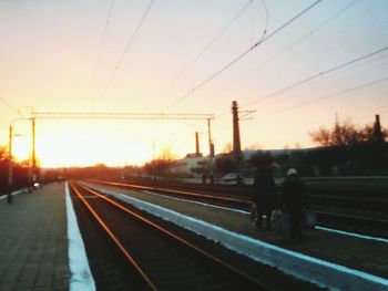 Silhouette people on railroad tracks against sky during sunset