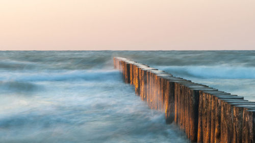 Wooden posts in sea against clear sky