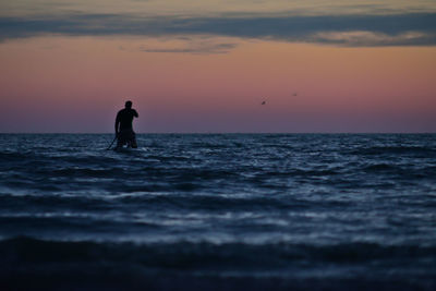 Silhouette man walking in sea against sky during sunset