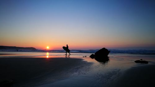 Silhouette man on beach against clear sky during sunset