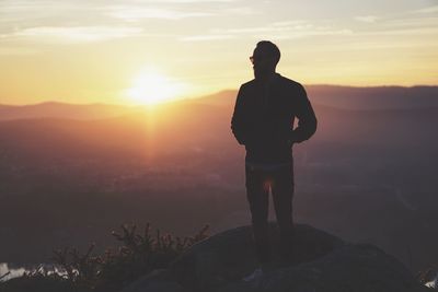 Silhouette man standing on mountain against sunset sky