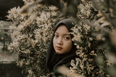 Portrait of young woman standing against plants