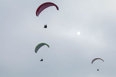 Low angle view of people paragliding against sky