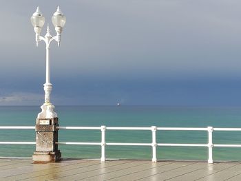 Street light on pier by sea against sky