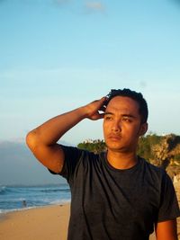 Portrait of young man standing at beach against sky
