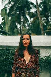 Portrait of beautiful young woman standing against plants