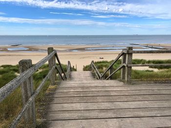 Boardwalk leading towards sea against sky