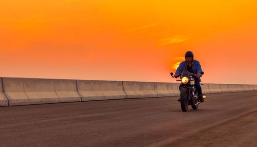 Man riding motorcycle on road against orange sky