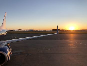 Airplane on runway against sky during sunset