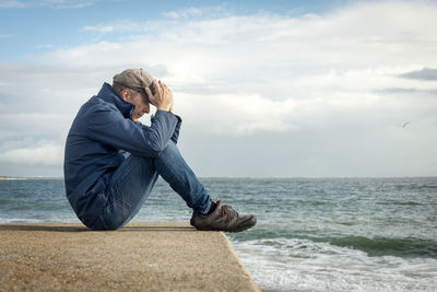 Man sitting by the sea with his head in his hands, emotions, mental health concept
