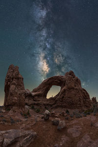 Unrecognizable traveler admiring breathtaking view of turret arch located near rough canyon against glowing milky way at night sky in arches national park in utah, usa