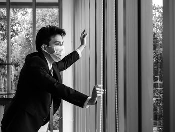 Side view portrait of young man standing against window