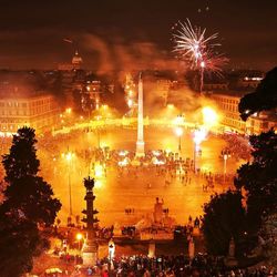 Firework display over illuminated city against sky at night