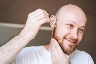 Adult handsome man with pipette with beard oil in bathroom at home