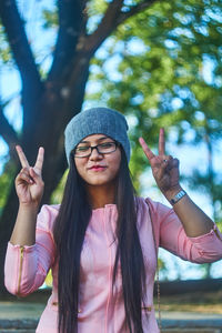 Portrait of young woman showing peace sign while standing at park