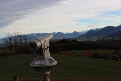 Coin-operated binoculars on field by mountains against sky