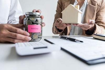 Midsection of agent holding model home while buyer with coins on table