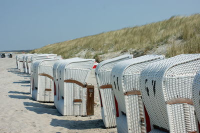 Hooded beach chairs on sand against clear sky