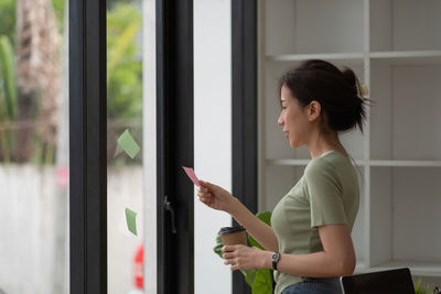 Side view of young woman looking through window