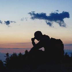 Silhouette person on rock by sea against sky during sunset