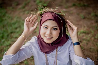 Portrait of smiling young woman in hijab wearing wreath on field