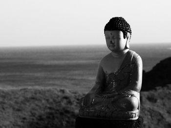 Close-up of buddha statue by sea against clear sky