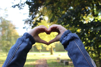 Midsection of man making heart shape against trees