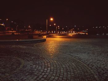 Illuminated street by buildings against sky at night