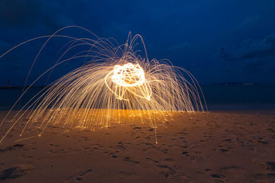 Illuminated light painting over sand at beach against sky during night