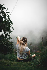 Rear view of woman sitting on field against foggy weather