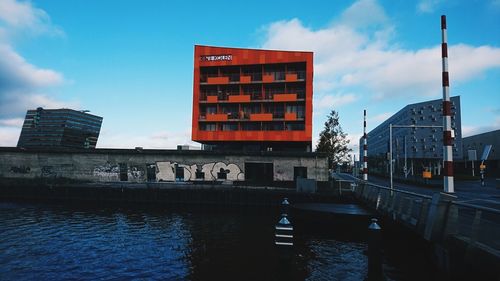 Information sign by river in city against sky