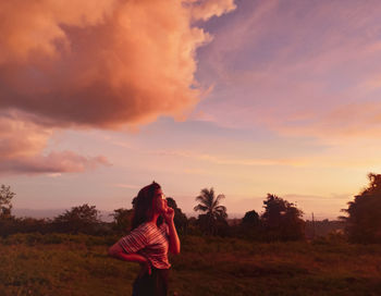 Woman standing on field against sky during sunset