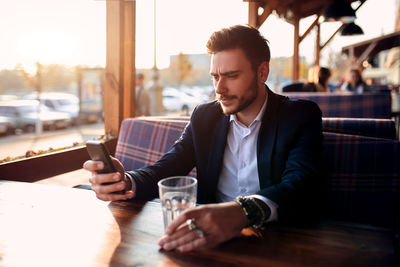 Handsome young man using phone while sitting on table at restaurant