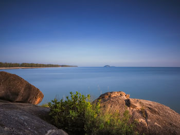 Rocks by sea against clear blue sky