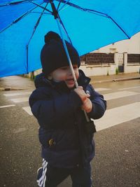 Rear view of boy holding umbrella while standing in city