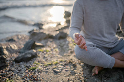 Low section of man meditating while sitting on beach