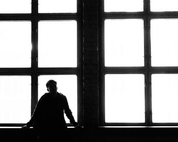 Rear view of silhouette man standing against window