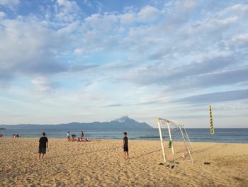 Children playing soccer at beach against sky