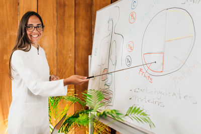 Female nutritionist standing in front of the white board smiling and explaining meal plan 