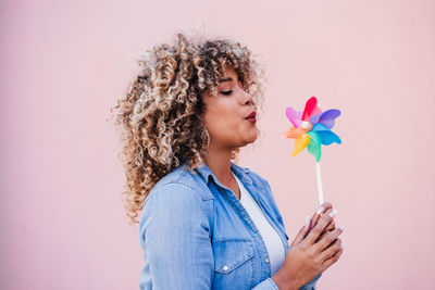 Beautiful happy hispanic woman with afro hair holding colorful pinwheel. pink background,wind energy