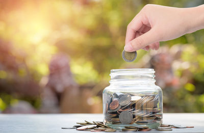 Cropped hand putting coin in jar on table